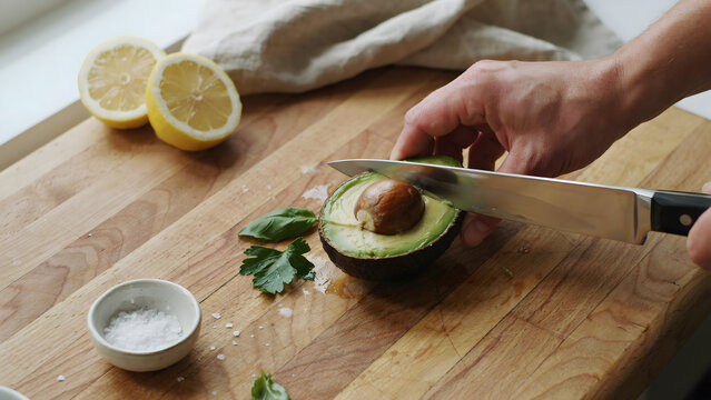 A chef slicing a ripe avocado on a rustic wooden cutting board with lemons