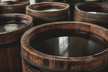 Fototapeta premium Wooden barrels filled with a dark liquid are displayed in a dimly lit setting, likely a cellar or aging room.