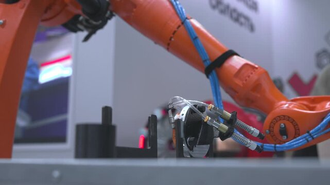 Orange industrial robotic arm spanning technical workstation with blue cable routing, compact tool head, glossy metal joints, diagonal composition, shallow focus, magenta accent light, modern