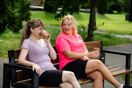 Friends enjoy coffee together on a park bench during a sunny afternoon