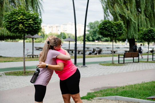 Friends meet and hug by the lake during a cloudy day in a city park