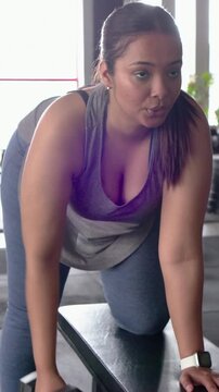 Vertical video: Picking up hex dumbbell woman pulling rows at gym bench in sportswear for strength