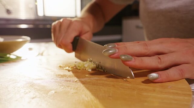 Woman Minces Fresh Garlic with Sharp Kitchen Knife on Wooden Board, Homemade Cooking and Aromatic Ingredient Preparation