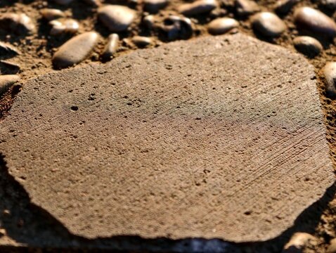 Rough flat stone slab surface texture surrounded by small river pebbles under natural sunlight