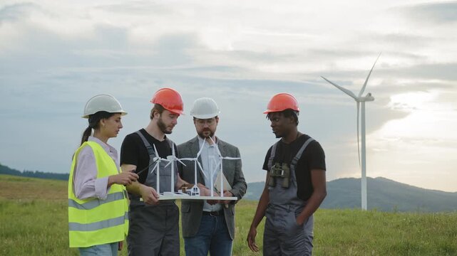 A diverse team of engineers examines wind turbine models at scenic wind farm. Their collaboration highlights renewable energy development, clean electricity, and sustainable innovation for industry