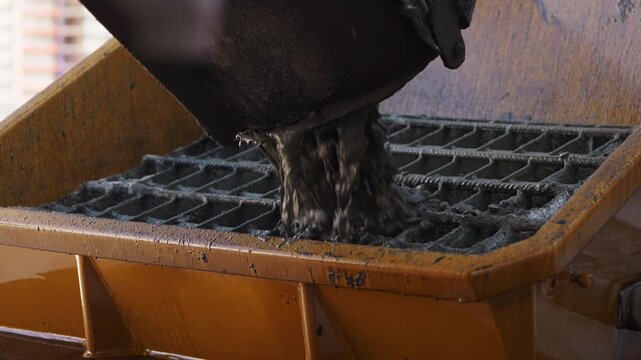 Pouring fresh concrete through grate into concrete pump hopper close up
