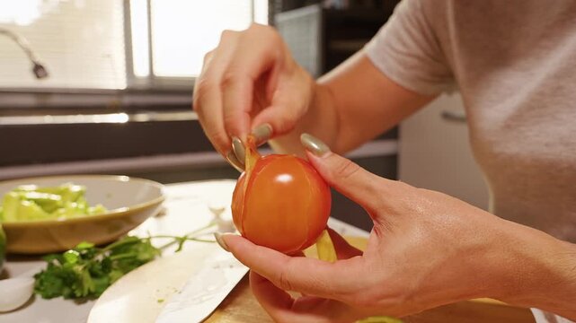 Hands Peel a Fresh Tomato Beside Avocado and Cilantro on a Kitchen Counter, Showing Fresh Food Preparation and Healthy Eating