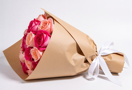 Pink peach rose bouquet wrapped in brown kraft paper tied with white satin ribbon on white studio background