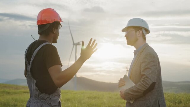 Two engineers shake hands near wind turbines at sunset. Their partnership reflects renewable energy innovation, clean electricity, and sustainable technology driving modern industry and environmental