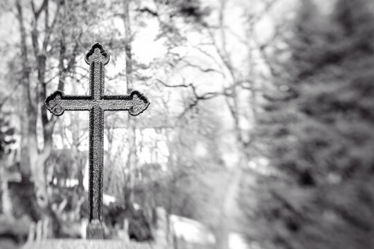 Old iron cross in cemetery. Black and white image. Selective focus, tilt shift, partly blurred. Ancient tombstone detail.