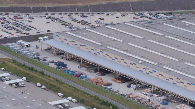 WODZISLAW SLASKI, POLAND - JULY 25, 2026: Aerial view of a massive modern industrial manufacturing plant, warehouse building, outdoor storage yard with pallets and materials, and a large employee car 