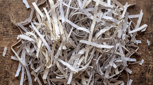 Close-up of shredded paper waste with printed text and letters scattered on a textured wooden surface.