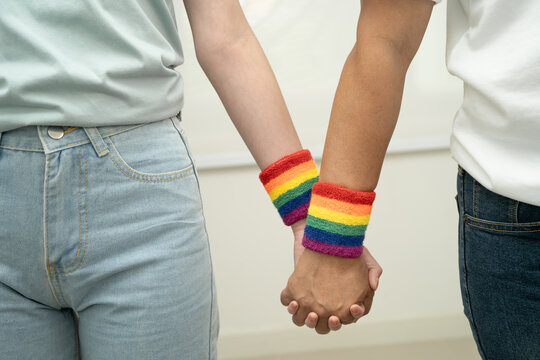Asian LGBT couple woman holding hand wearing rainbow wristband.