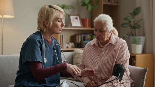 Middle aged Caucasian female nurse measuring blood pressure of senior Caucasian woman using digital tonometer at home. Clip is ideal for geriatric care, home nursing, and medical services ads