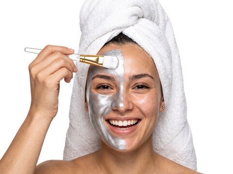 Woman applying silver face mask with brush, smiling, towel on head, skincare routine