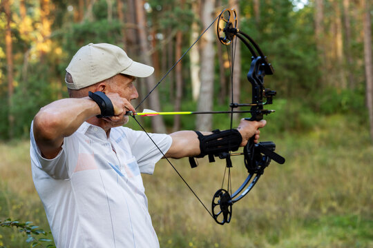 Senior man practicing archery with compound bow in forest