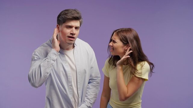 Young couple pointing to their ears with confused expressions, signaling they cannot hear clearly. Communication problems, listening difficulty, audio issues, misunderstanding and attention cues.