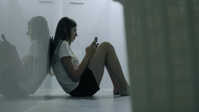 Lonely generation z schoolgirl using smartphone sitting indoors.