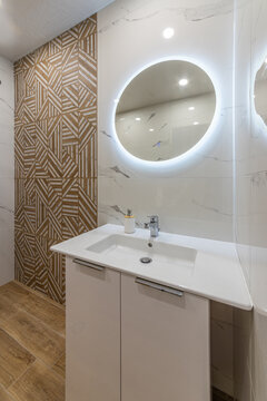 Modern bathroom interior design with a white ceramic sink, and round illuminated LED mirror. Luxurious and clean space.