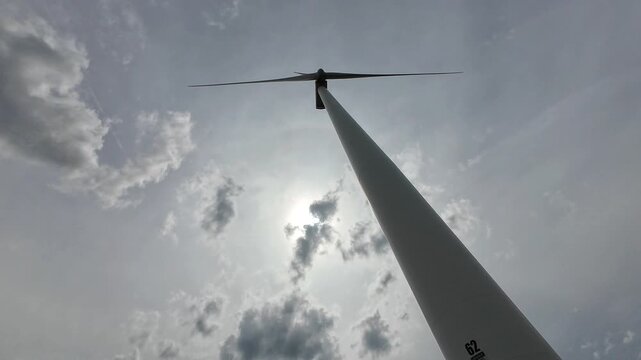 A wide low-angle shot embracing the vastness of the sky and the height of the turbine. The lighting creates a serene yet powerful mood for global warming solutions.