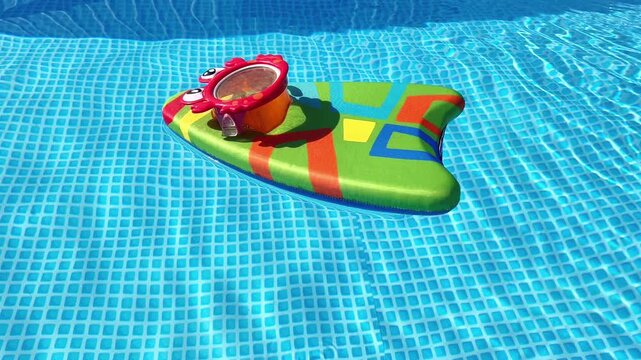 Bright colorful kid kickboard floating on clear blue water in a backyard swimming pool on a sunny summer day.