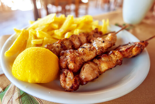 Grilled chicken skewers with fries and lemon in Greece