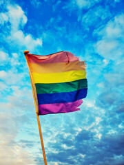 Rainbow pride flag waving against a blue cloudy sky © Roxana