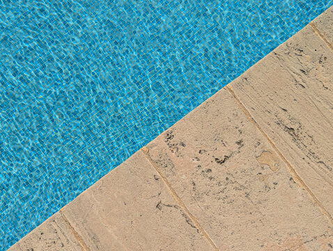 Pool water with blue mosaic tiles next to a textured natural stone edge