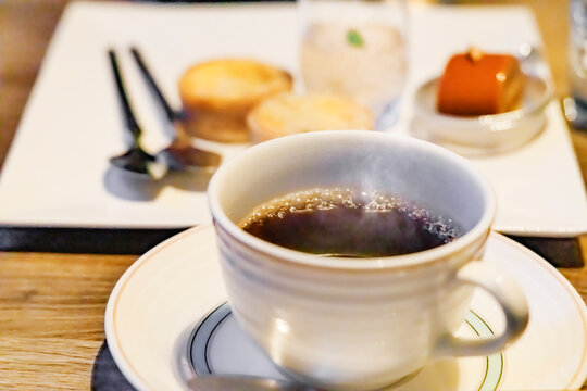 温かいホットコーヒーと奥に見えるスイーツプレート