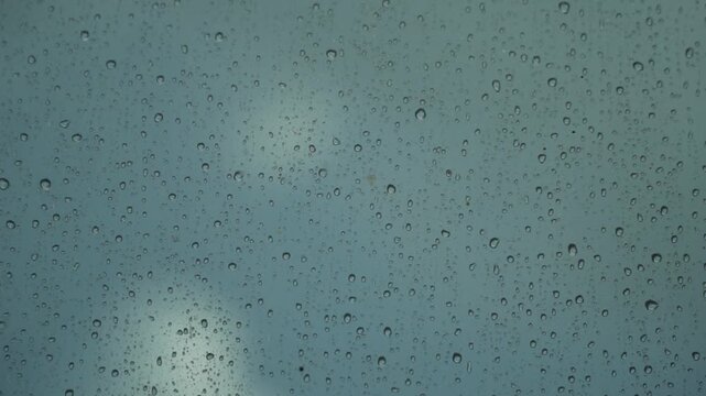 Close-up view of countless rain droplets adhering to a transparent glass surface during a cloudy day, creating a beautiful textured background for design