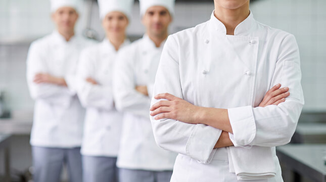 Confident chef with crossed arms leading a blurred culinary team in a bright commercial kitchen, ideal for restaurant branding.