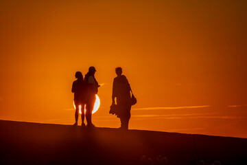 Fototapeta premium Saint-Aubin-Sur-Mer, France - 07 27 2026: View silhouettes of people backlight on the jetty at the beach with the sea and the sun behind at golden hour