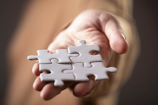 Close-up of a hand holding connected white puzzle pieces, symbolizing teamwork, collaboration, problem solving, partnership, strategy, support, unity, business success, and finding solutions.
