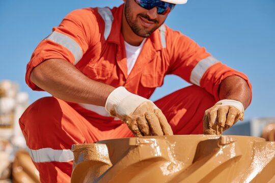 Worker inspecting mud covered tricone drill bit