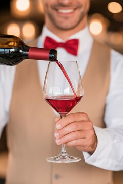 Sommelier pouring red wine into glass with warm bokeh background