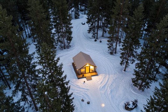 Cabin surrounded by trees in snow during winter evening