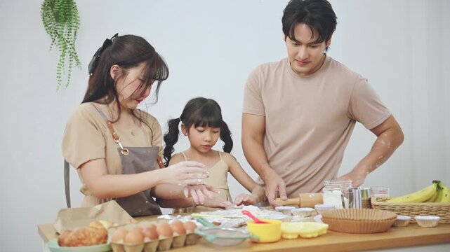 Happy Asian family baking together in kitchen, parents and daughter preparing homemade cookies at home. Concept of parenting, learning activity for kids, family bonding, and home lifestyle.