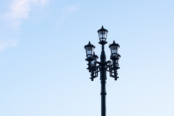 A vintage street lamp with four lanterns against a clear blue sky. The lamp is black and ornate, adding charm to the urban landscape. © Ksu
