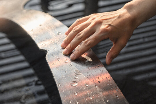 Close up view of a hand touching a smooth wet surface covered with water droplets in warm sunlight