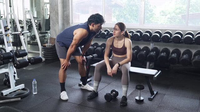 Personal trainer coaching a young woman during a dumbbell workout in a modern gym, promoting strength training, fitness, healthy lifestyle and professional exercise guidance.