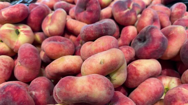 Close-up of fresh flat peaches, also known as donut or Saturn peaches, piled together with red and yellow skin. Fresh fruit, summer harvest, healthy food
