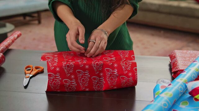 Close-up of hands wrapping a gift in bright red paper with tape and scissors.