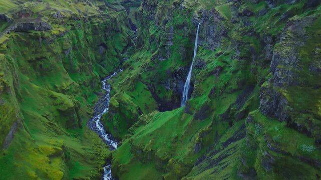 Cinematic drone flight through the lush Mulagljufur Canyon revealing towering moss-covered cliffs, cascading waterfalls and a winding river deep within Iceland&rsquo;s spectacular Highlands.