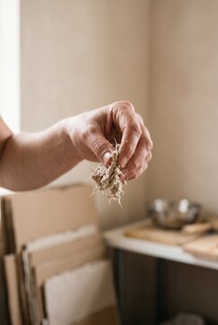Craftsperson holding a piece of wet raw paper pulp fiber during the handmade papermaking process in an artisan workshop studio
