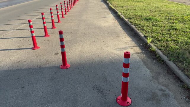 Row of red and white striped traffic bollards on asphalt road, safety delineator posts for traffic control, outdoor urban infrastructure, transportation