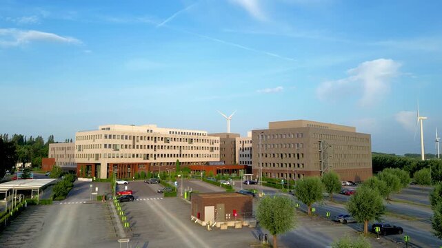 Aerial view of a modern corporate headquarters with wind turbines, showcasing sustainability and green energy. Cinematic drone establishing shot of a business park campus.