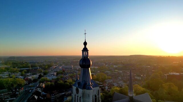 Cinematic aerial footage of Aarschot church tower at sunrise, revealing the Belgian cityscape in warm morning light.