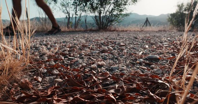 Shadow of a solo traveler walking on a dusty gravel path at golden hour, low angle ground view of dry grass and leaves, conceptual journey and exploration