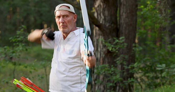 Senior man practicing recurve archery in forest during outdoor training