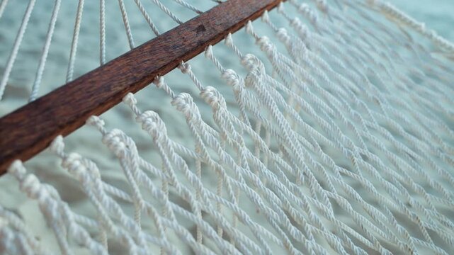Hammock webbing features thick natural cordage strands woven into a durable pattern attached to a wooden crossbar, which creates a relaxing outdoor structure for leisure seekers to rest comfortably.